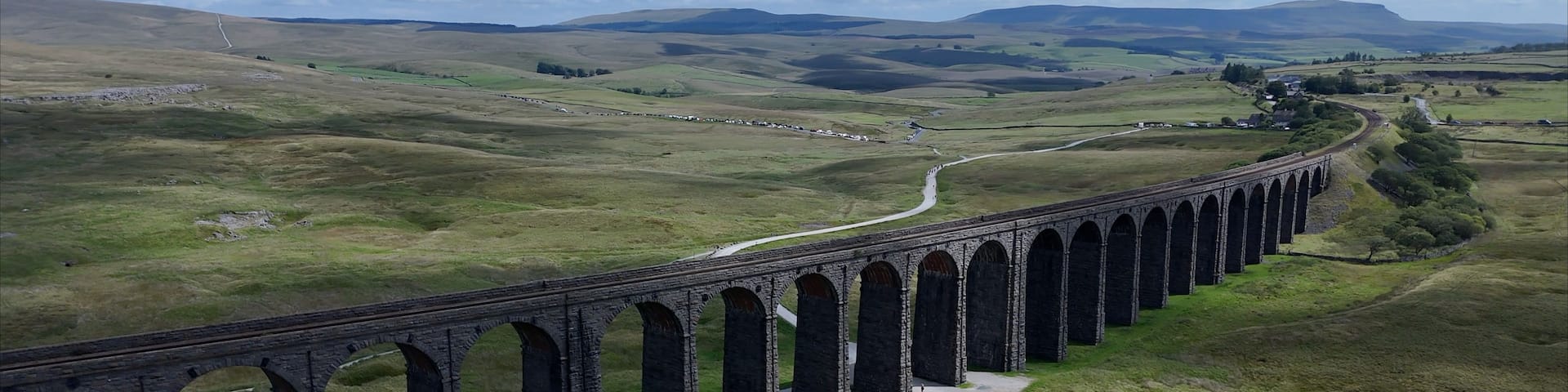 A long viaduct spanning a valley with a winding road beside it.
