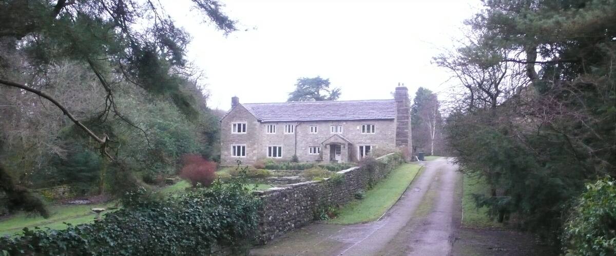 A stone house with a paved driveway and a stone wall on one side.