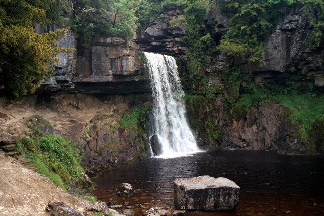 A waterfall cascading into a river surrounded by rocky cliffs and greenery.