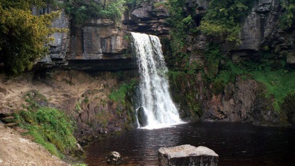 A waterfall cascading into a river surrounded by rocky cliffs and greenery.