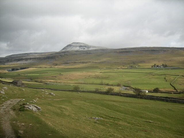 A rural landscape with a prominent hill, stone walls, and a small building.