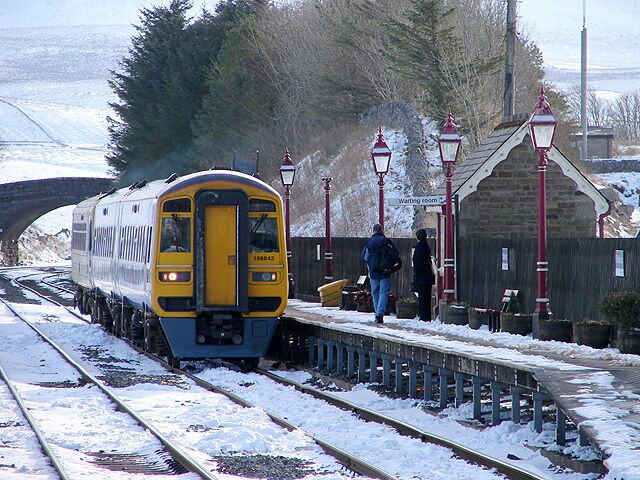 A train at a snowy station with a bridge in the background.