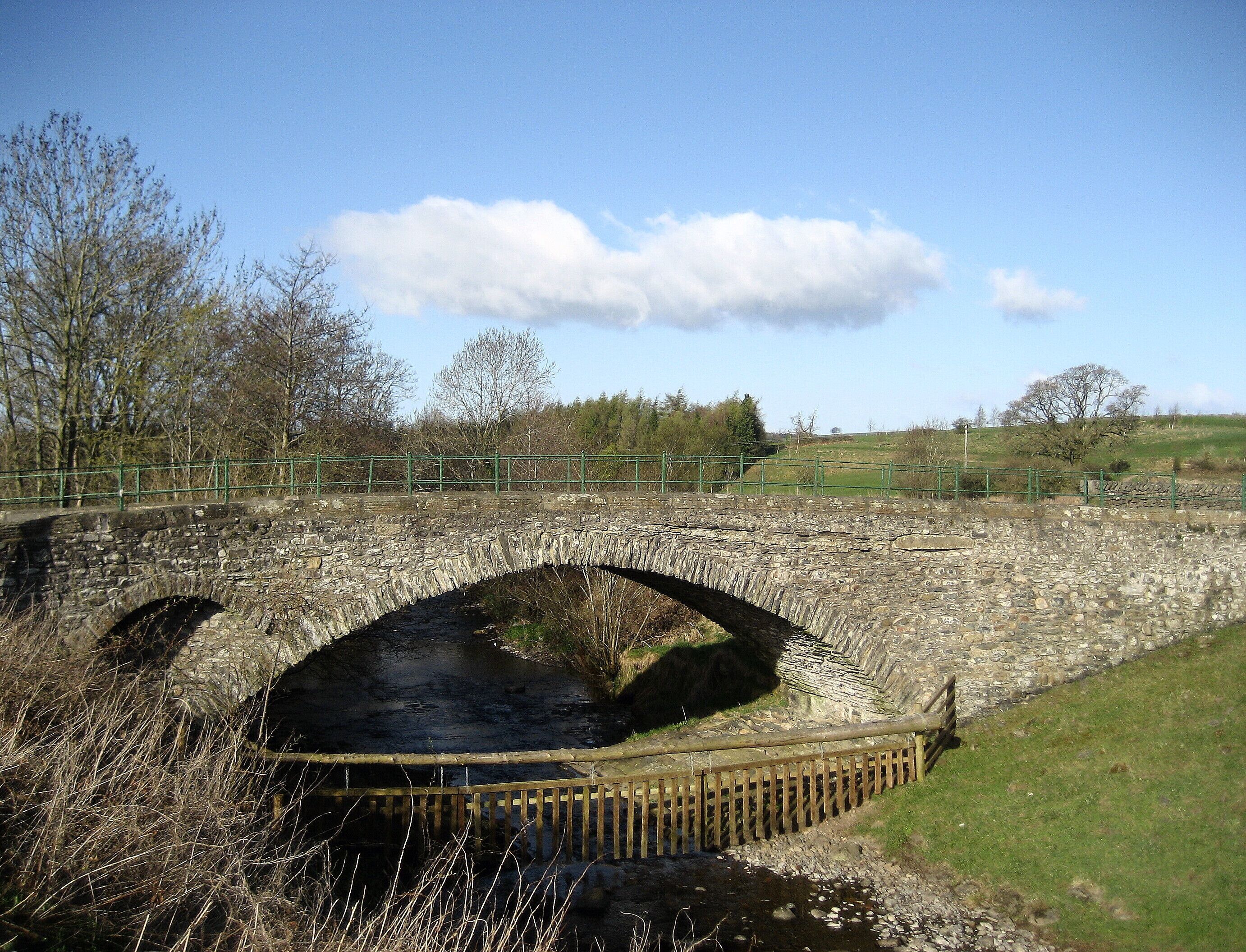A stone bridge over a river with a wooden fence in the foreground.