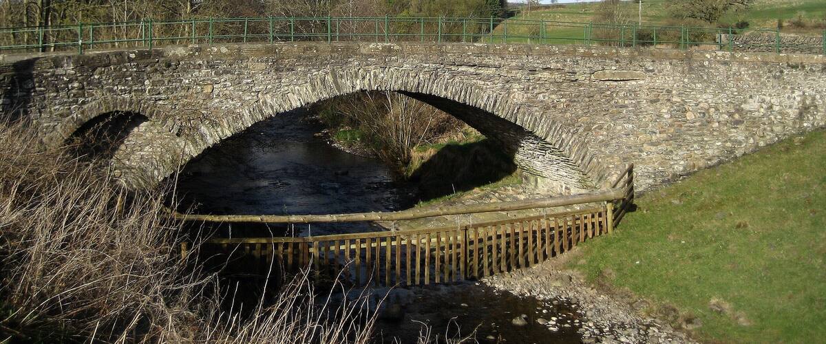 A stone bridge over a river with a wooden fence in the foreground.