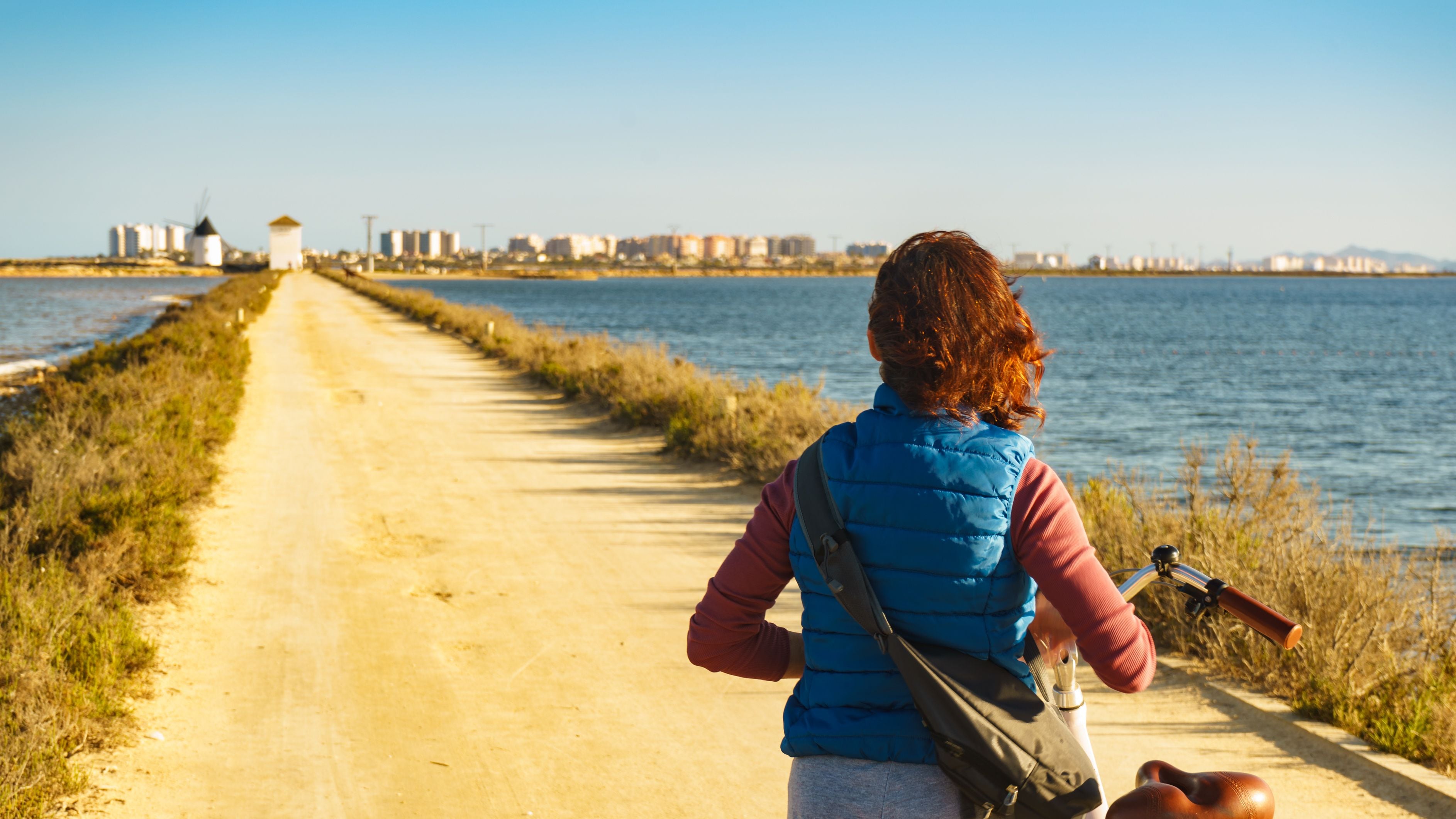 A woman walking on a coastal path with a cityscape in the background.