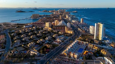 Paisagem costeira com um porto de iates, edifícios altos e um céu azul claro.
