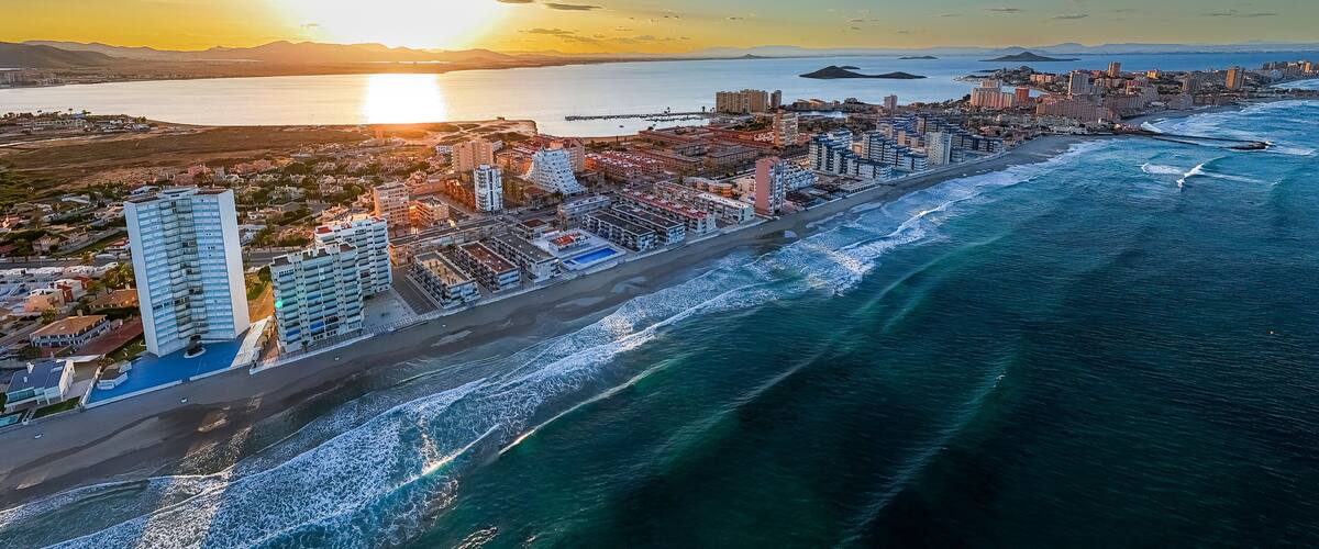 A coastal cityscape with a prominent beachfront, high-rise buildings, and a sunset over the ocean.