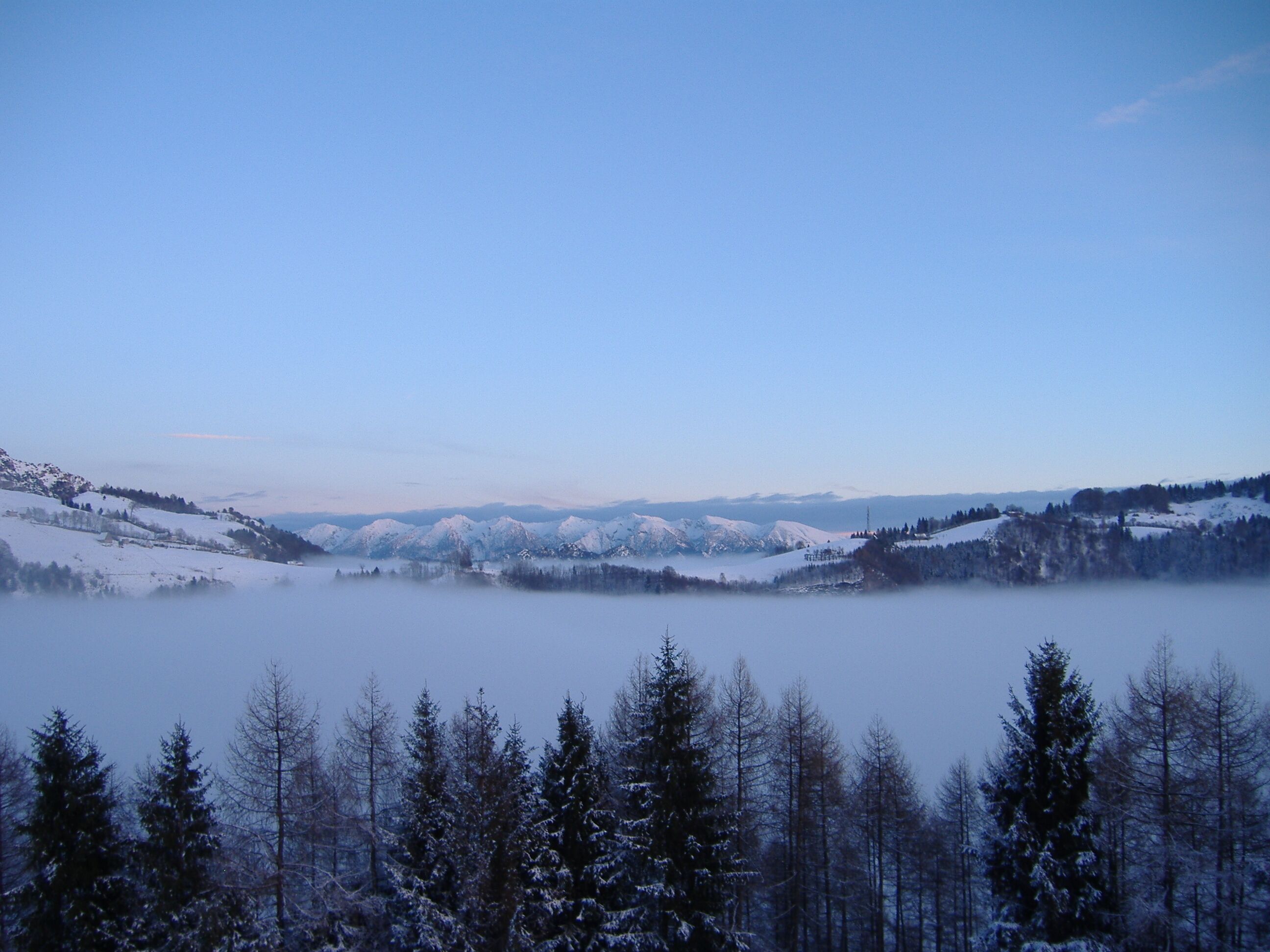 Scatto dagli altipiani di Denai, siti nel Parco regionale Alto Garda Bresciano, con vista sugli altipiani di Cima Rest, il monte Puria (1474 m s.l.m.) e la catena del Baldo sullo sfondo. La nebbia ricopre il fondo valle della Val Vestino.