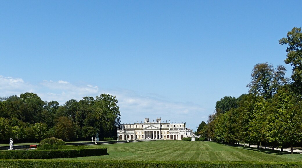 A large, classical building with a symmetrical facade, surrounded by well-manicured hedges and trees.
