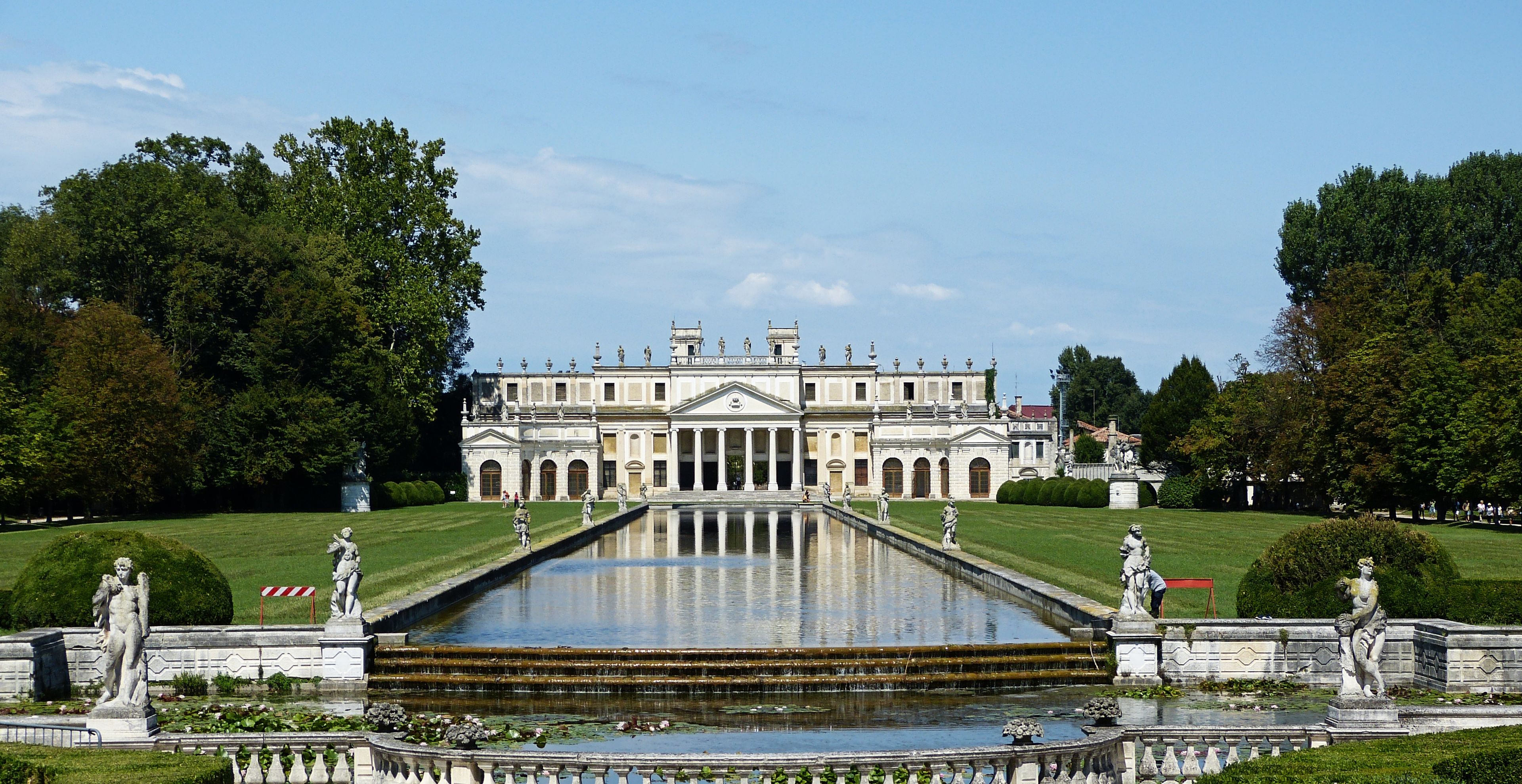 A grand palace with a symmetrical facade, a central fountain, and statues lining the pathways.