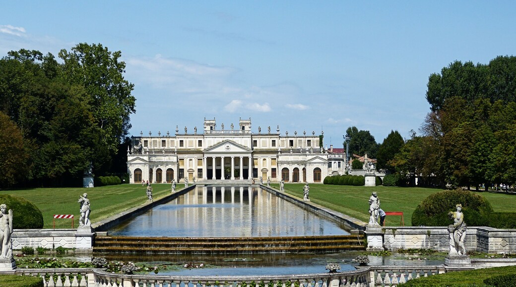 A grand palace with a symmetrical facade, a central fountain, and statues lining the pathways.