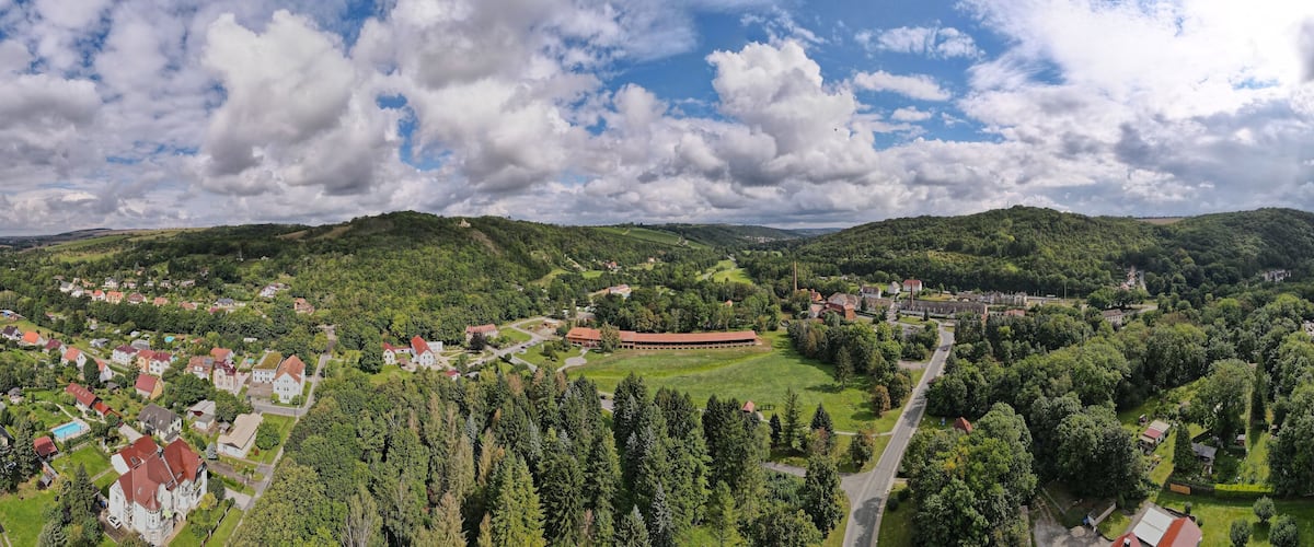 A town nestled in a valley with rolling hills, surrounded by dense forests and a large open field.