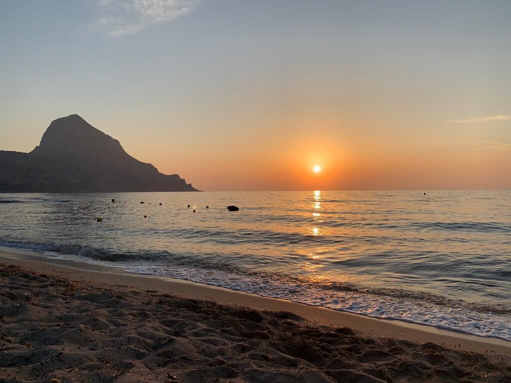 A beach at sunset with a mountain in the background.