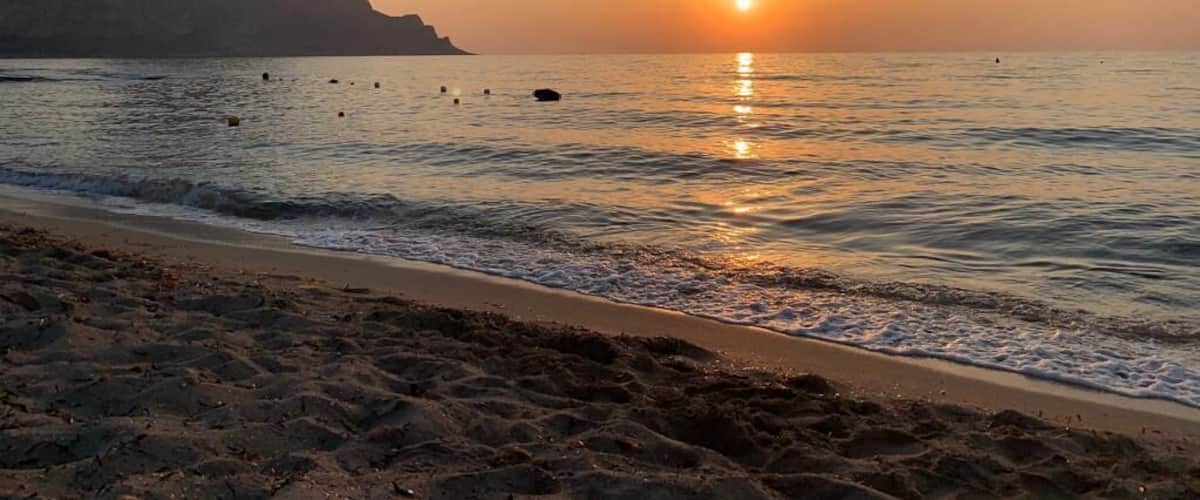 A beach at sunset with a mountain in the background.