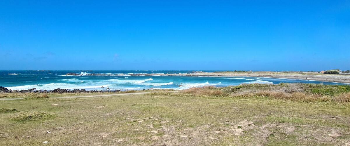 A coastal landscape with rocky shores, waves crashing onto the beach, and a clear blue sky.