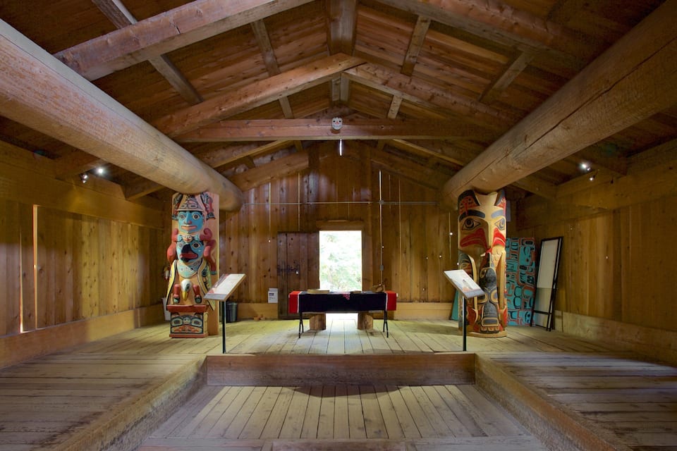 A wooden interior with a central table and two totem poles.