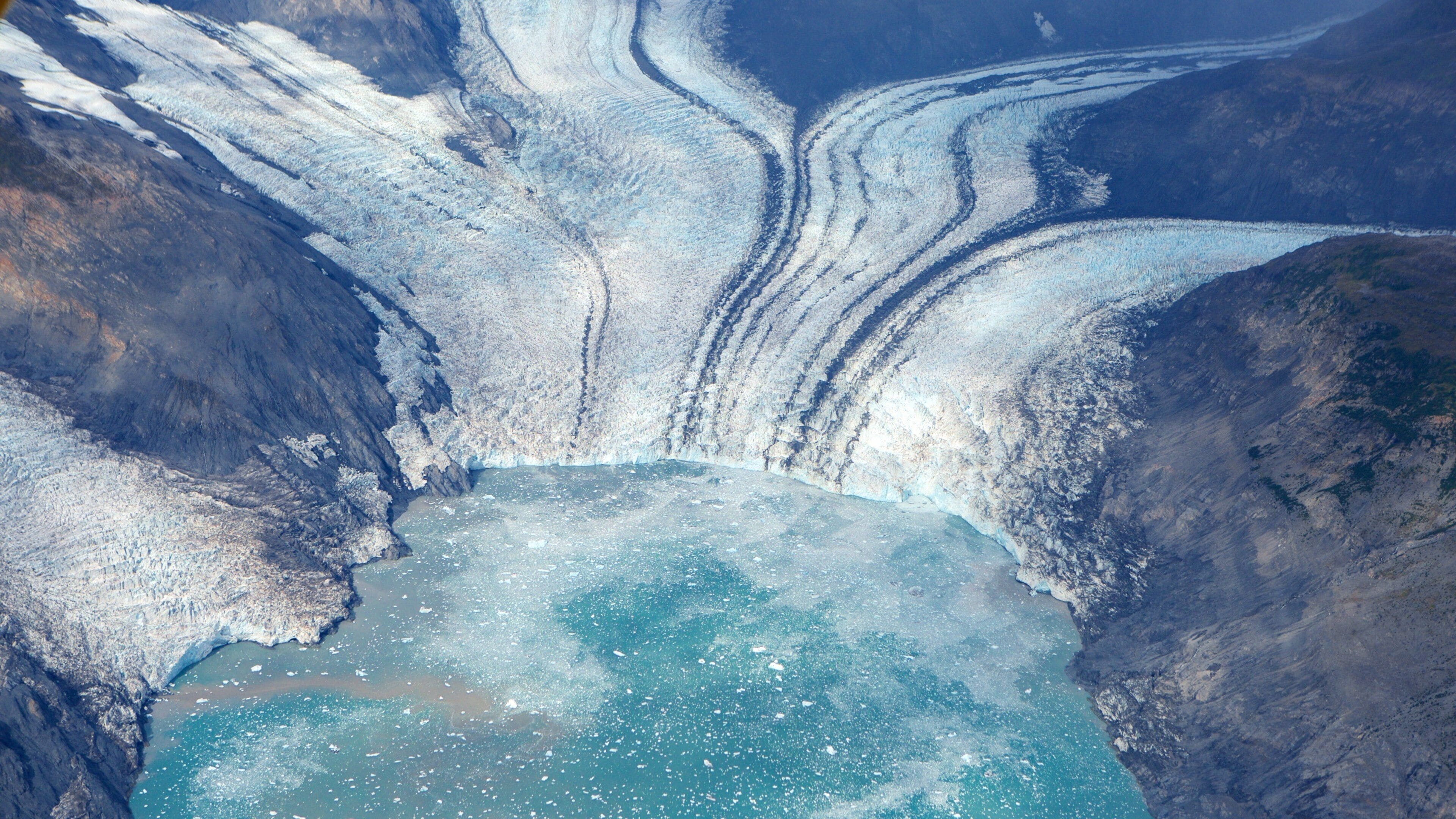 A glacier with a calving ice cliff and a partially frozen lake.