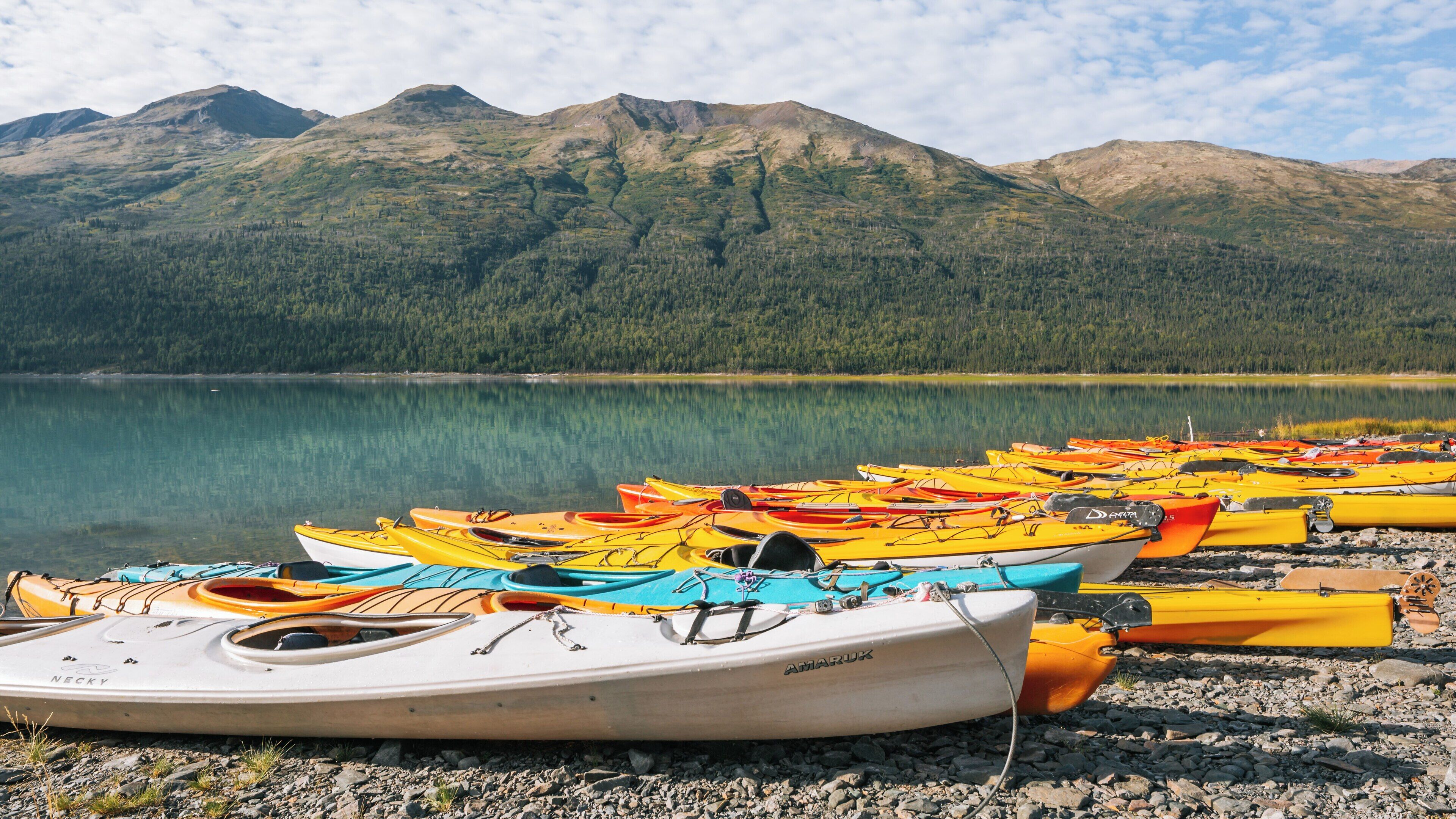 Bright kayaks line the shore of Eklutna Lake surrounded by stunning Alaskan mountains under a blue sky