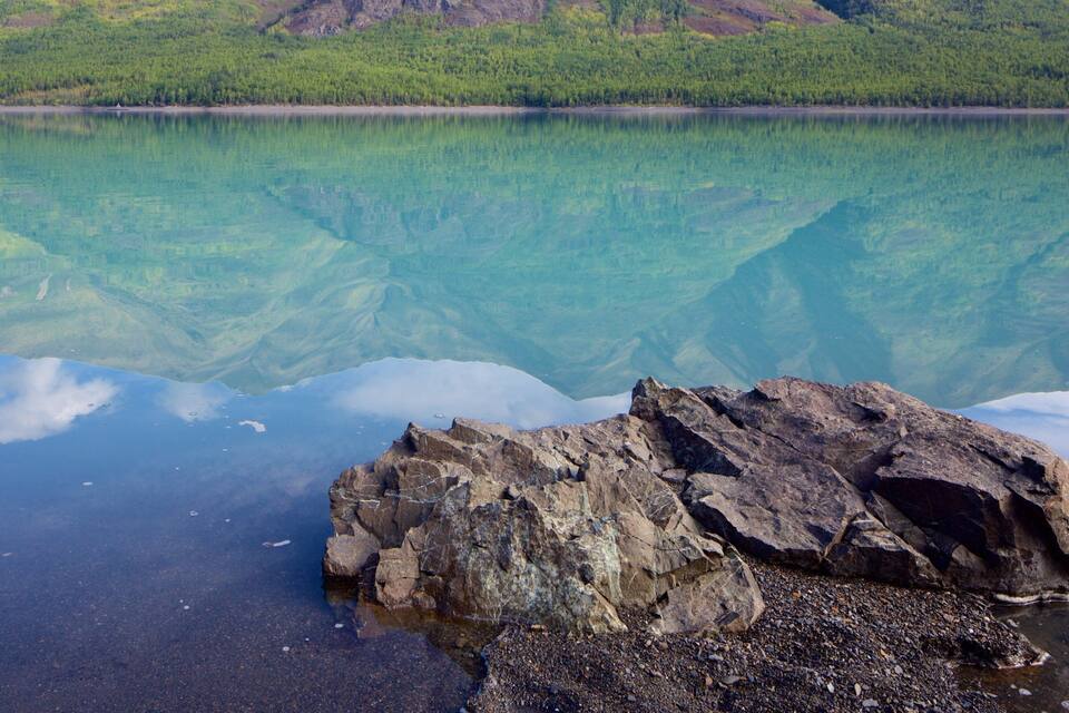 A clear lake with visible underwater rock formations and a rocky shoreline.