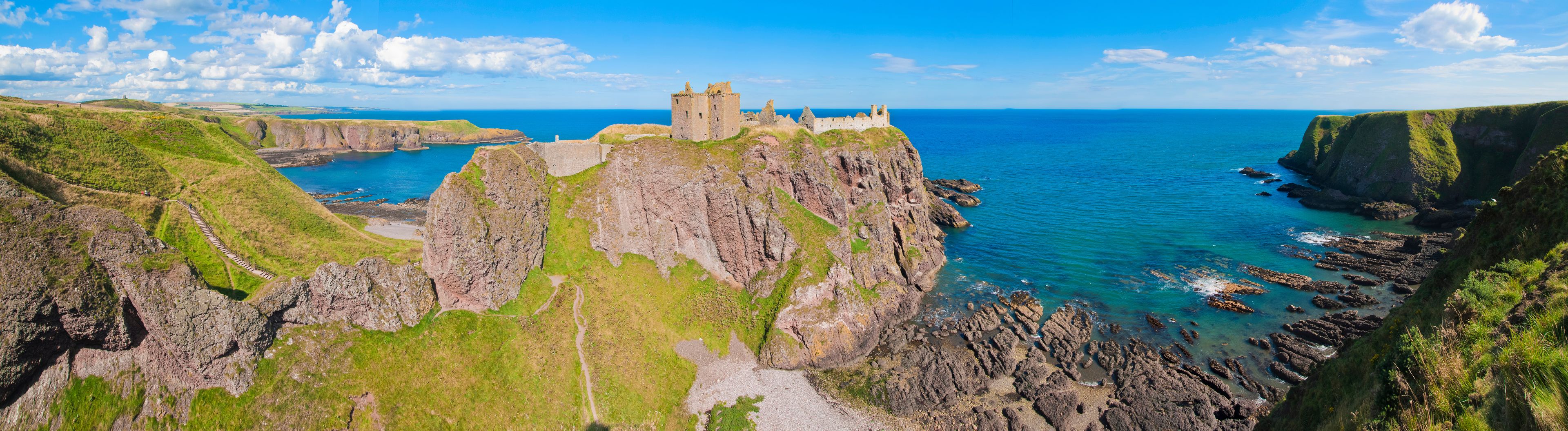 Panorama of a cliff with ancient castle in a bay with blue sky and white clouds in Dunnottar Castle, near Stonehaven, Aberdeenshire