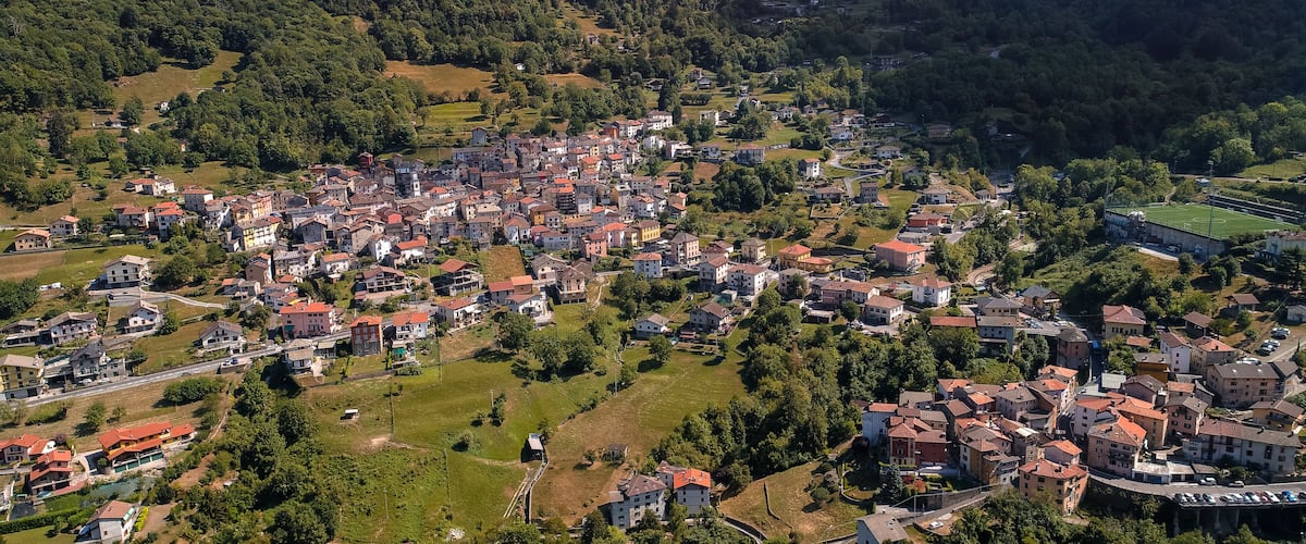 An aerial view of a densely populated town with numerous buildings, green spaces, and a sports field.