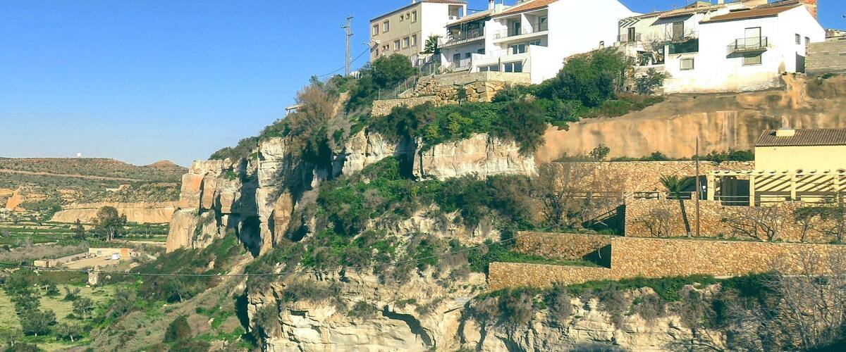 A hillside with buildings, rocky cliffs, and sparse vegetation.