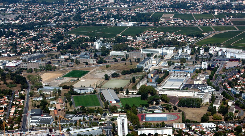 An aerial view of a city with residential areas, green fields, and several large buildings including a stadium.