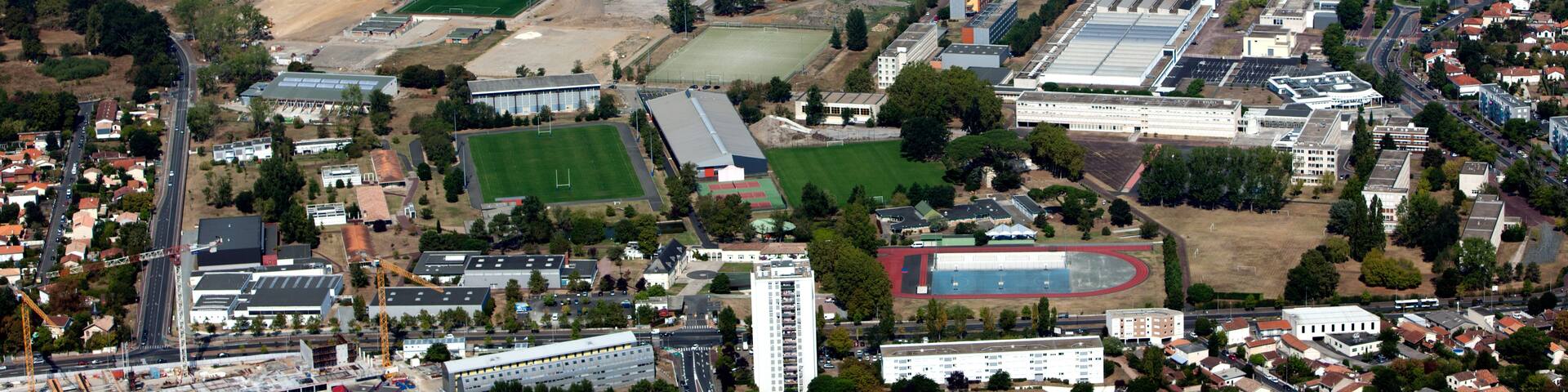 An aerial view of a city with residential areas, green fields, and several large buildings including a stadium.