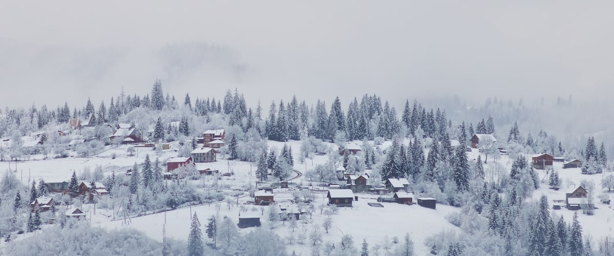 A snow-covered village with houses and trees on a hillside.