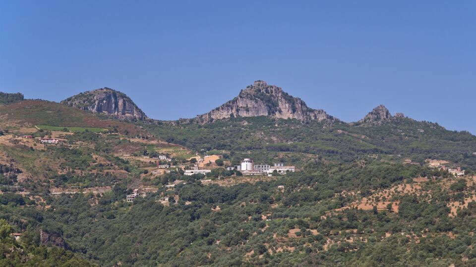 A mountainous landscape with a prominent rocky peak and a white building in the valley.