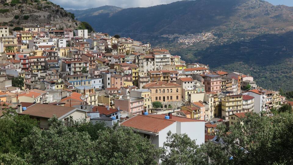A densely packed hillside town with colorful buildings, a mountain backdrop, and a clear sky.