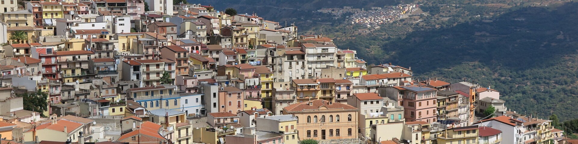 Un pueblo en una ladera densamente poblada, con edificios coloridos, telón de fondo montañoso y cielo despejado.
