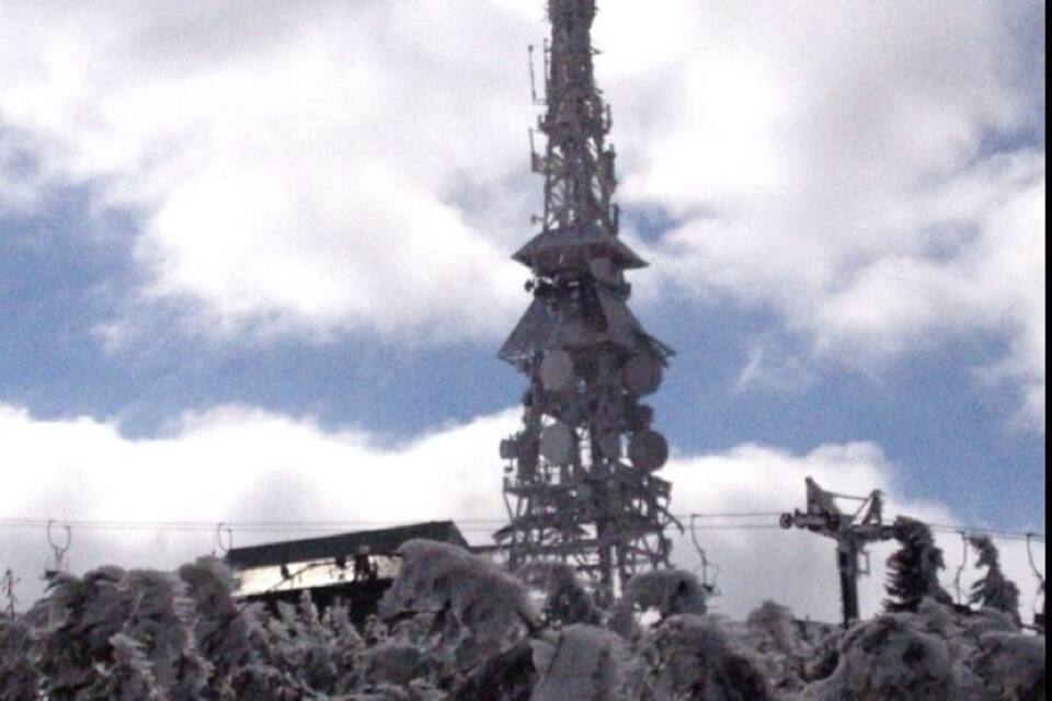 Une montagne enneigée, avec une haute tour de communication et un télésiège en arrière-plan.