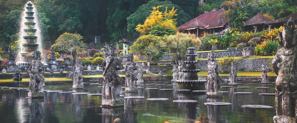 Un jardin paisible agrémenté d’une fontaine à étages, de statues en pierre et de bâtiments de style traditionnel.