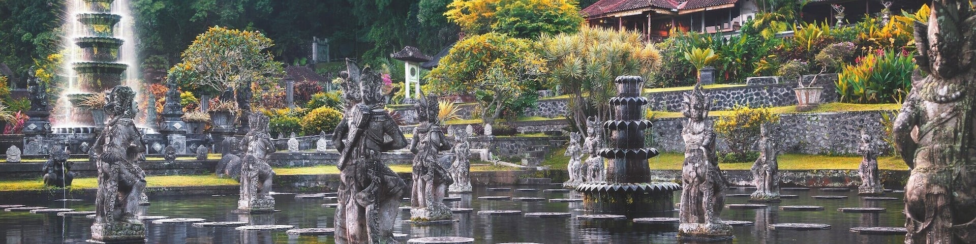 A serene garden with a tiered water fountain, stone statues, and traditional buildings.