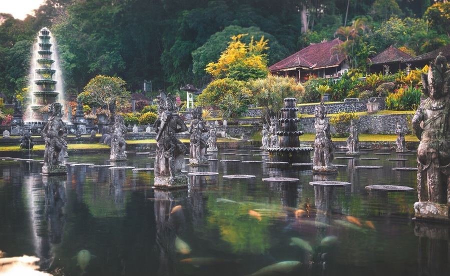 Een rustige tuin met een meerlaagse waterfontein, stenen beelden en traditionele gebouwen.