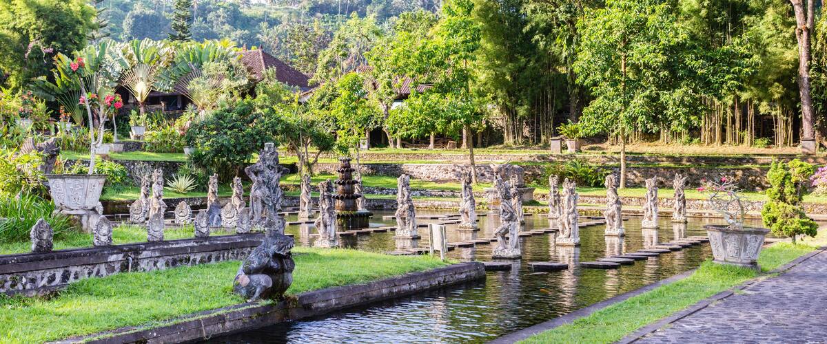 A serene garden with stone statues, a pond, and lush greenery.