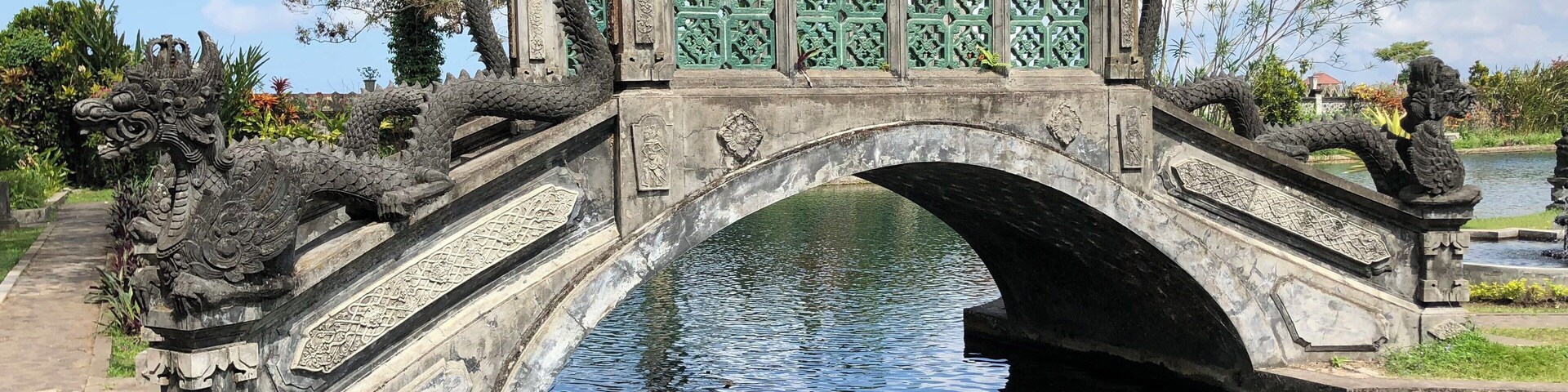 A stone bridge with dragon sculptures and a pond.