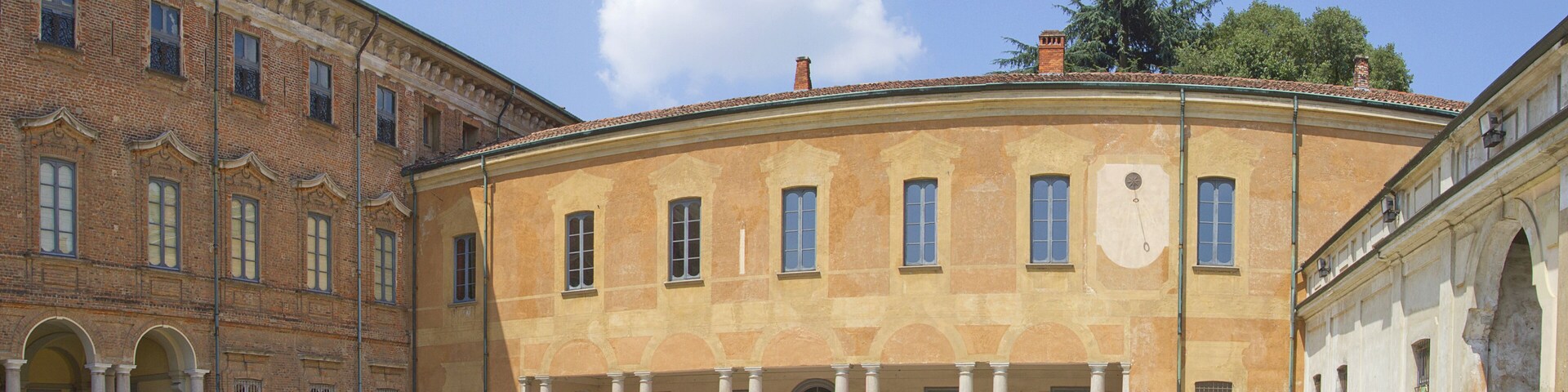 A courtyard with a yellow building featuring columns and arched doorways, surrounded by a cobblestone ground.