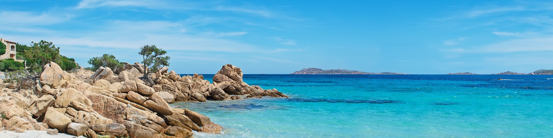 Un paisaje costero con aguas turquesas cristalinas, formaciones rocosas y una isla distante.