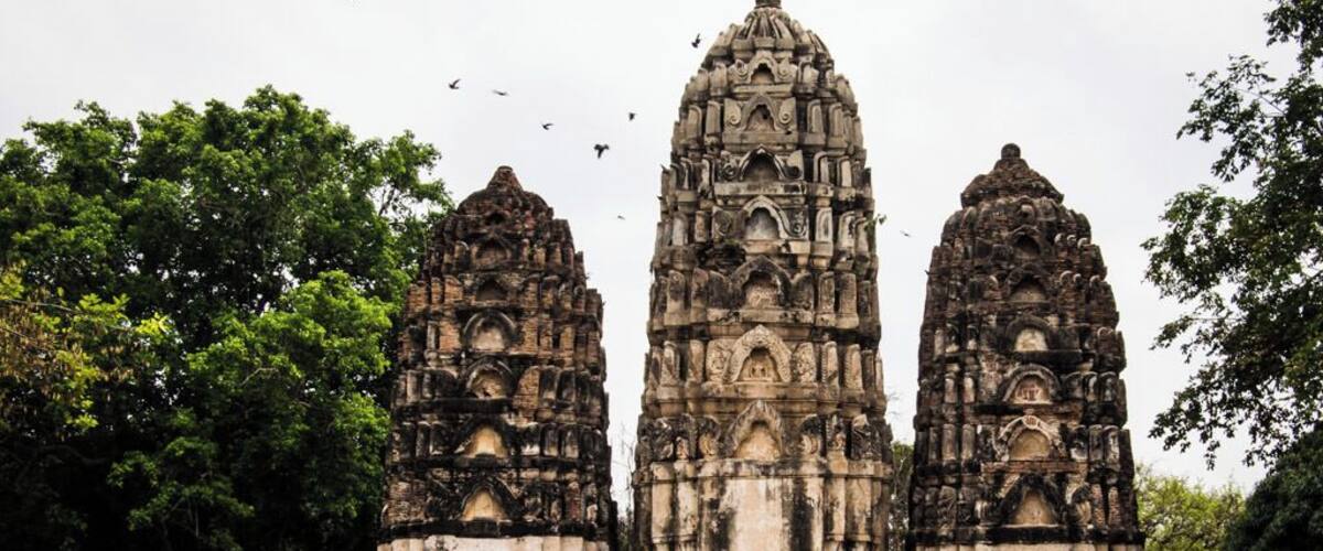 Un temple doté de trois tours, entouré d’arbres et d’un mur de briques.
