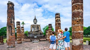 Happy family with one boy looking at a Buddha statue in an old temple
