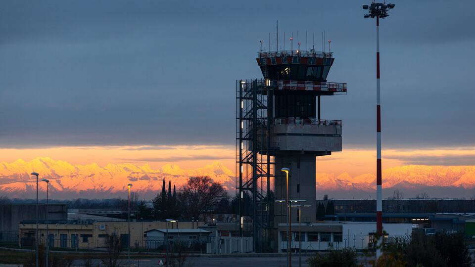 A control tower with a mountain range in the background during sunset.