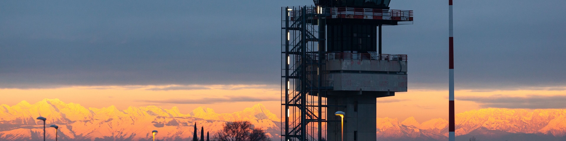 Airport control tower at Trieste airport during colorful sunset over city, Italy