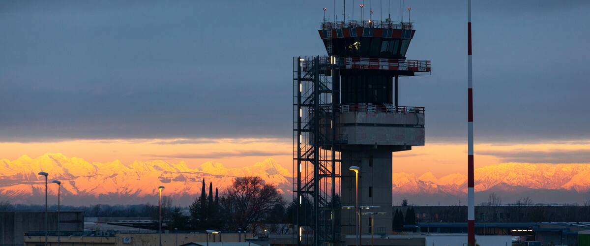 A control tower with a mountain range in the background during sunset.