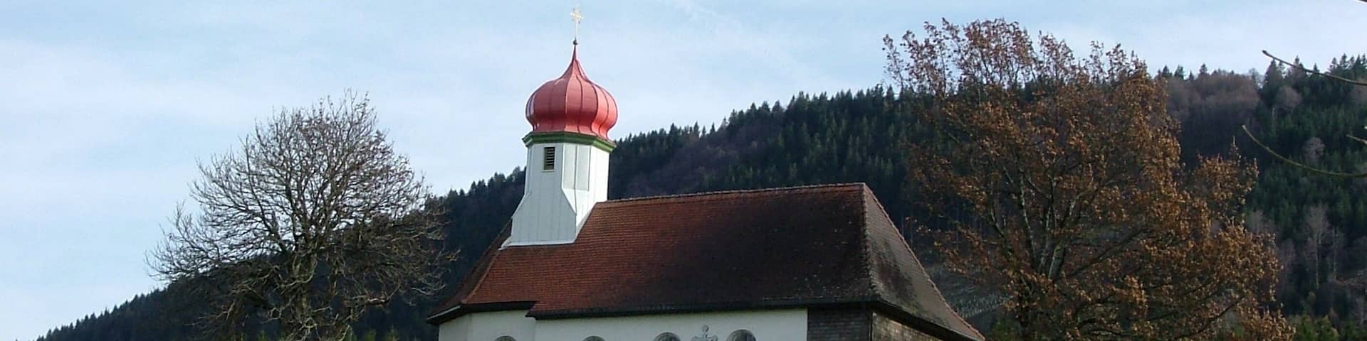 A white church with a red dome and a brick tower, surrounded by a green field and trees.