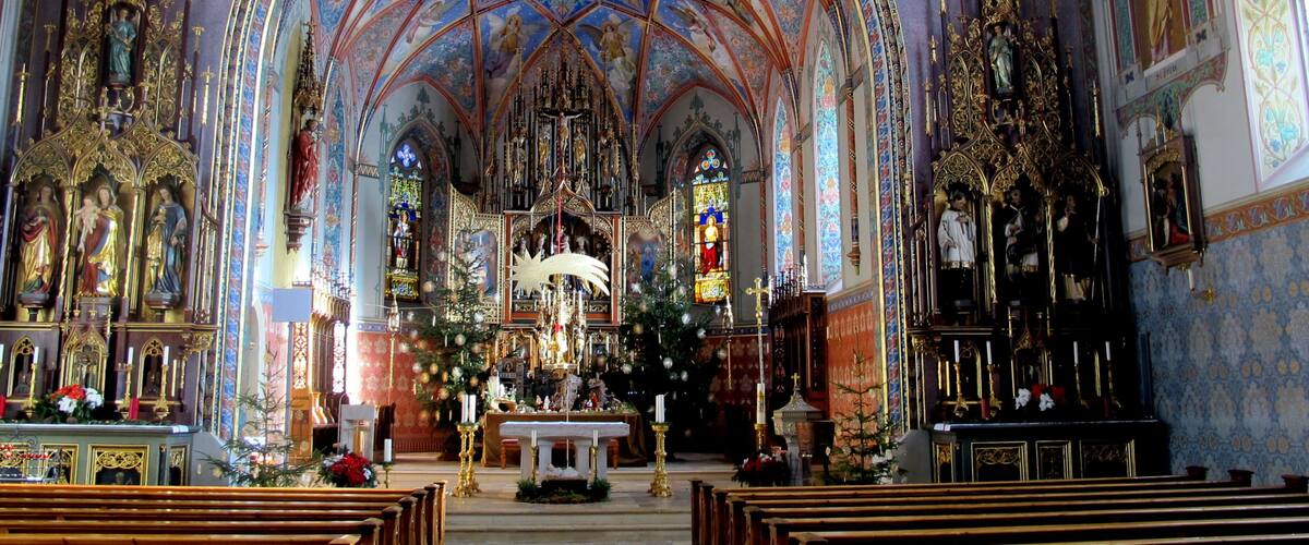 An ornate church interior with a high vaulted ceiling, stained glass windows, and religious statues.