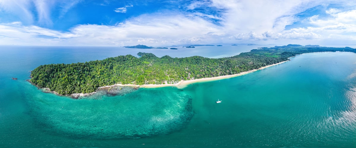A tropical island with a clear turquoise sea, a sandy beach, and dense green forest.