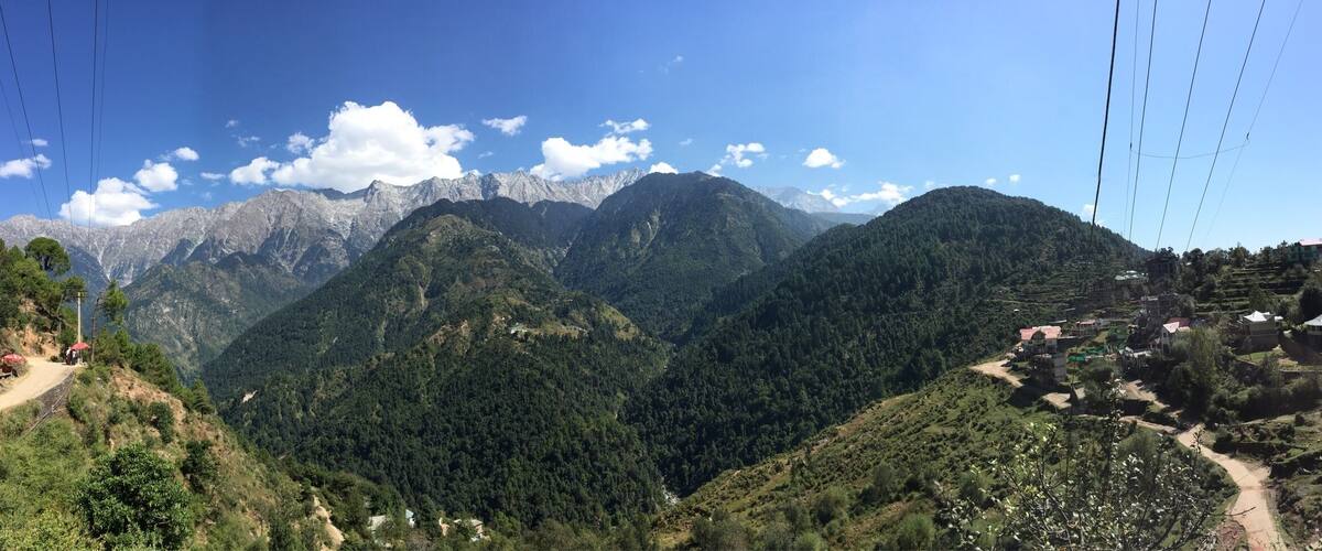 A mountainous landscape with a clear sky, a winding road, and a small settlement with houses.