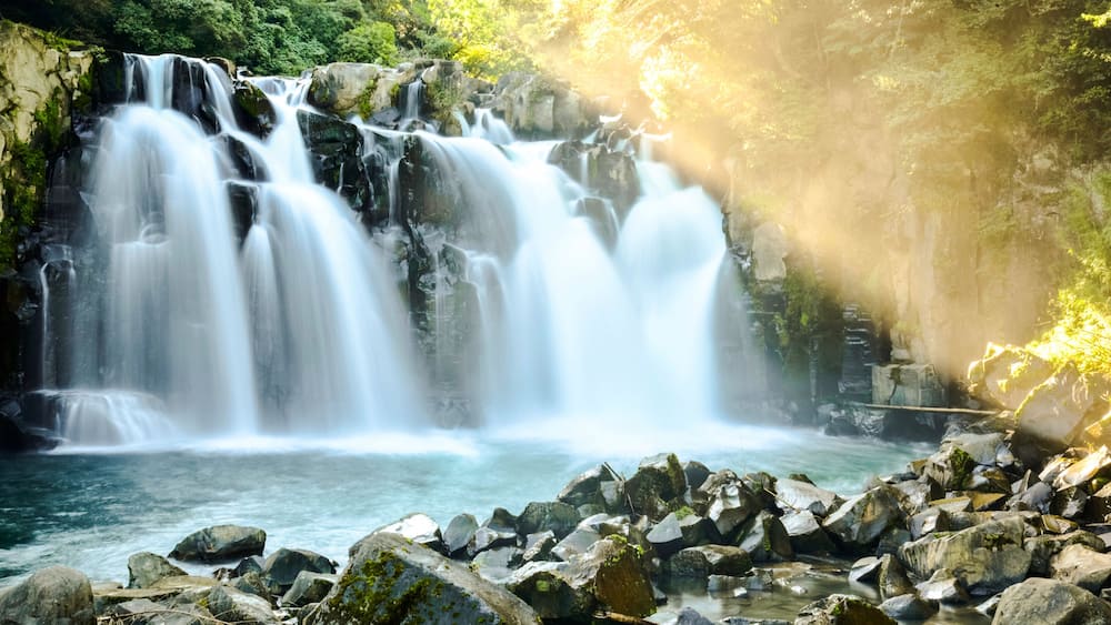 A waterfall cascading over rocks into a river, surrounded by lush greenery.